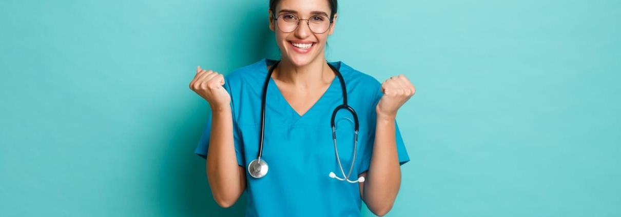 Smiling nurse holding her fists up against a solid backdrop